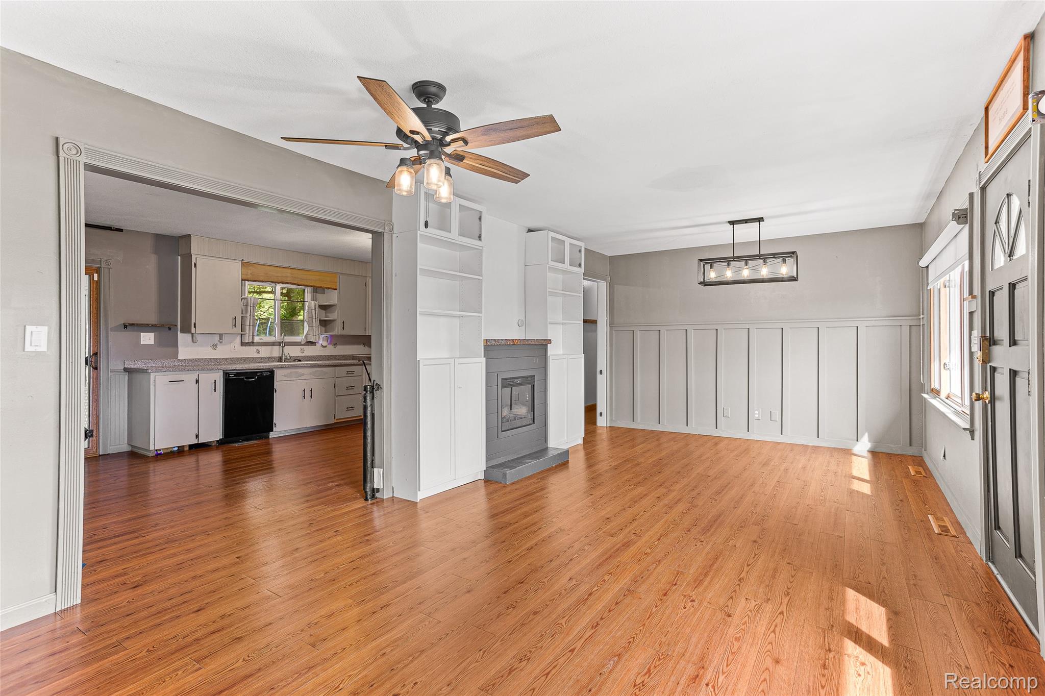 9561 Exeter Road Carleton, MI 48117 - Photo 16 of 46 Wood-finish flooring throughout, board and batten wall detailing, fireplace with built-in shelving, ceiling fan with integrated lighting, and an open concept kitchen with black appliances