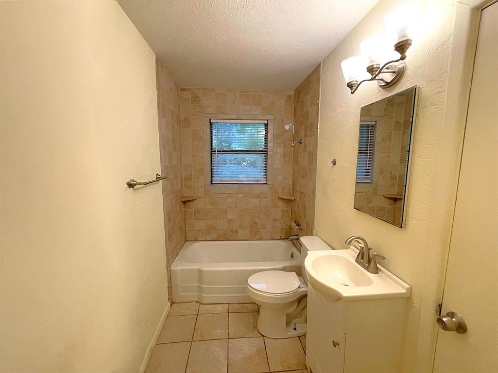 501 South Perry Avenue Denison, TX 75020 - Photo 6 of 11 Bathroom featuring a white vanity with integrated sink, tiled flooring, bathtub with subway tile surround, window with blinds, and a wall-mounted light fixture