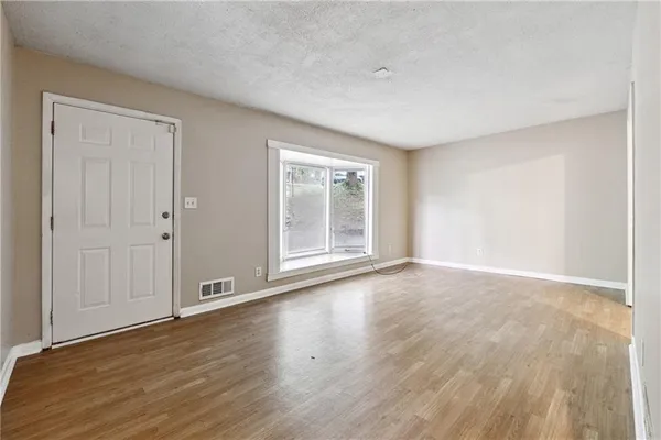 a view of an empty room with wooden floor and a window