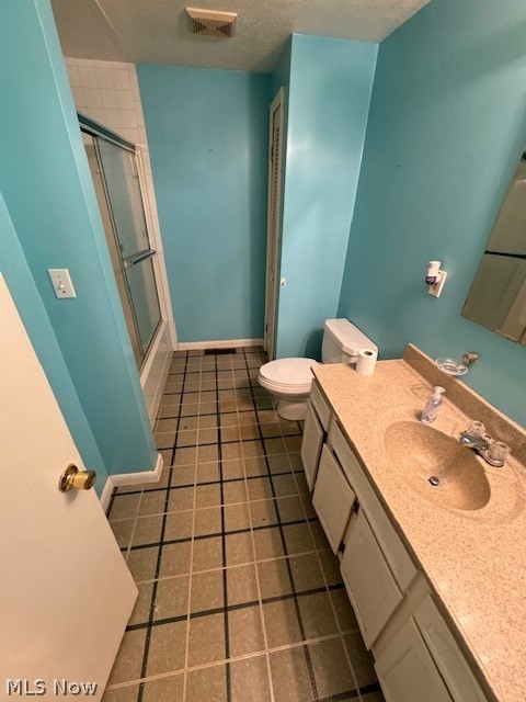 Bathroom with a shower with door, tile patterned floors, toilet, and vanity