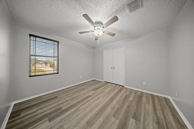 a view of an empty room with chandelier fan and wooden floor