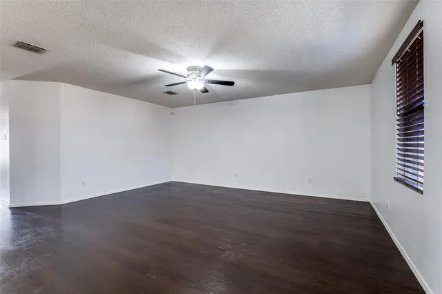 an empty room with wooden floor chandelier fan and windows