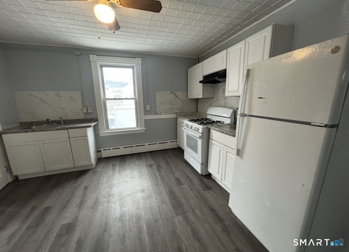 a kitchen with granite countertop a refrigerator a sink dishwasher a stove and white countertops with wooden floor