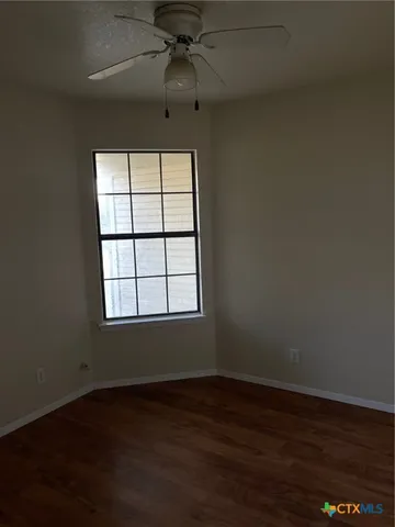 an empty room with wooden floor chandelier fan and windows