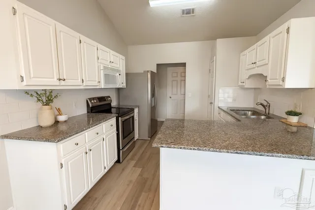 a kitchen with granite countertop a sink stainless steel appliances and white cabinets
