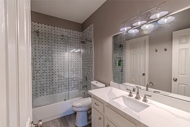 a bathroom with a granite countertop sink a toilet a mirror a bathtub and shower
