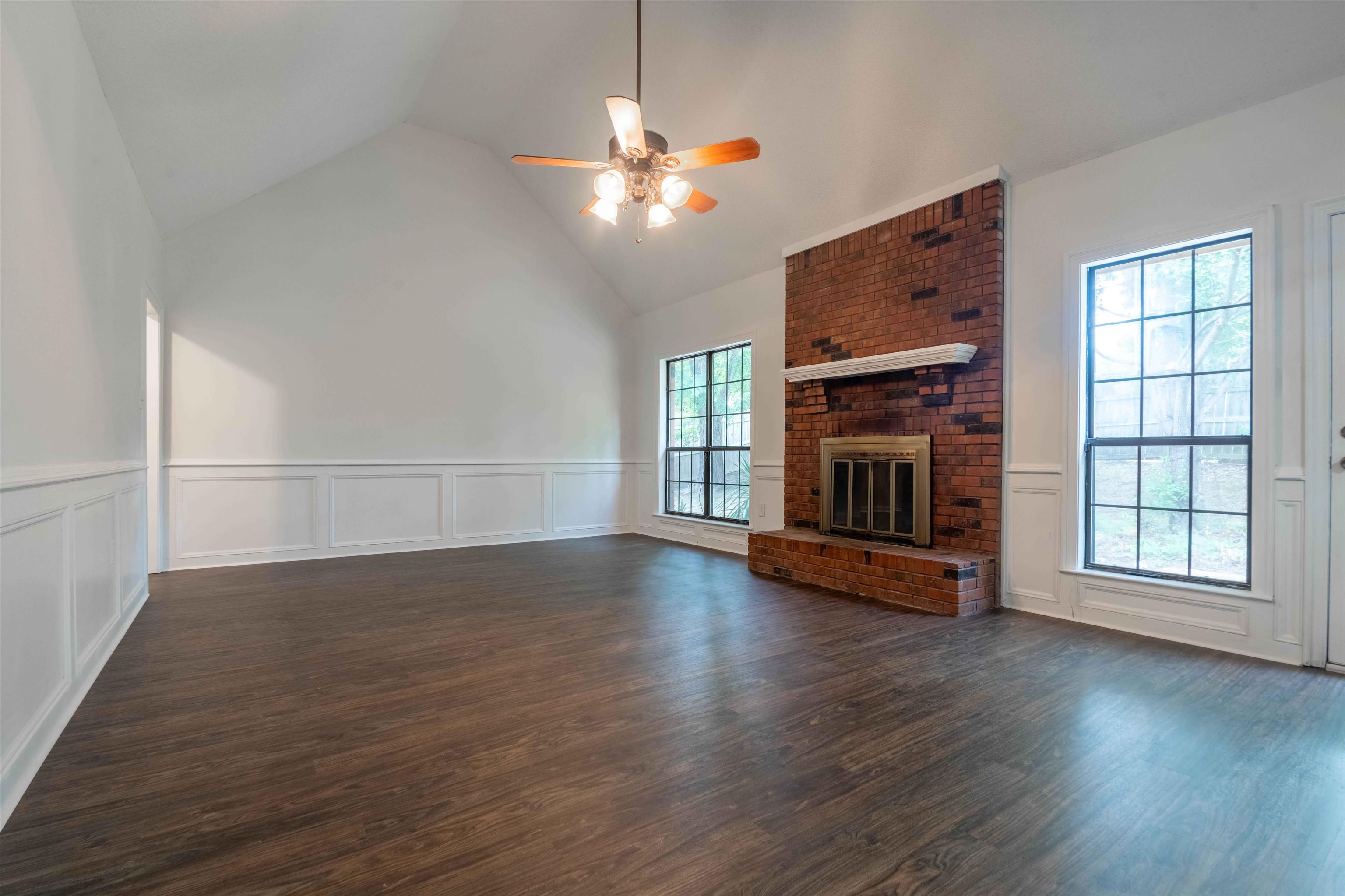 7800 Buck Ridge Cove Memphis, TN 38016 - Photo 10 of 36 Spacious room featuring vaulted ceilings, brick fireplace with mantel, wood-finish flooring, and white wainscoting