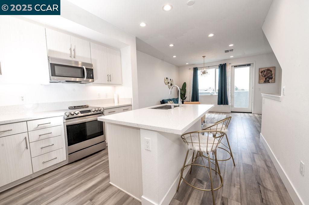 9877 MacArthur Boulevard, Unit E Oakland, CA 94605 - Photo 3 of 13 a kitchen with stainless steel appliances kitchen island granite countertop a stove a sink and a microwave