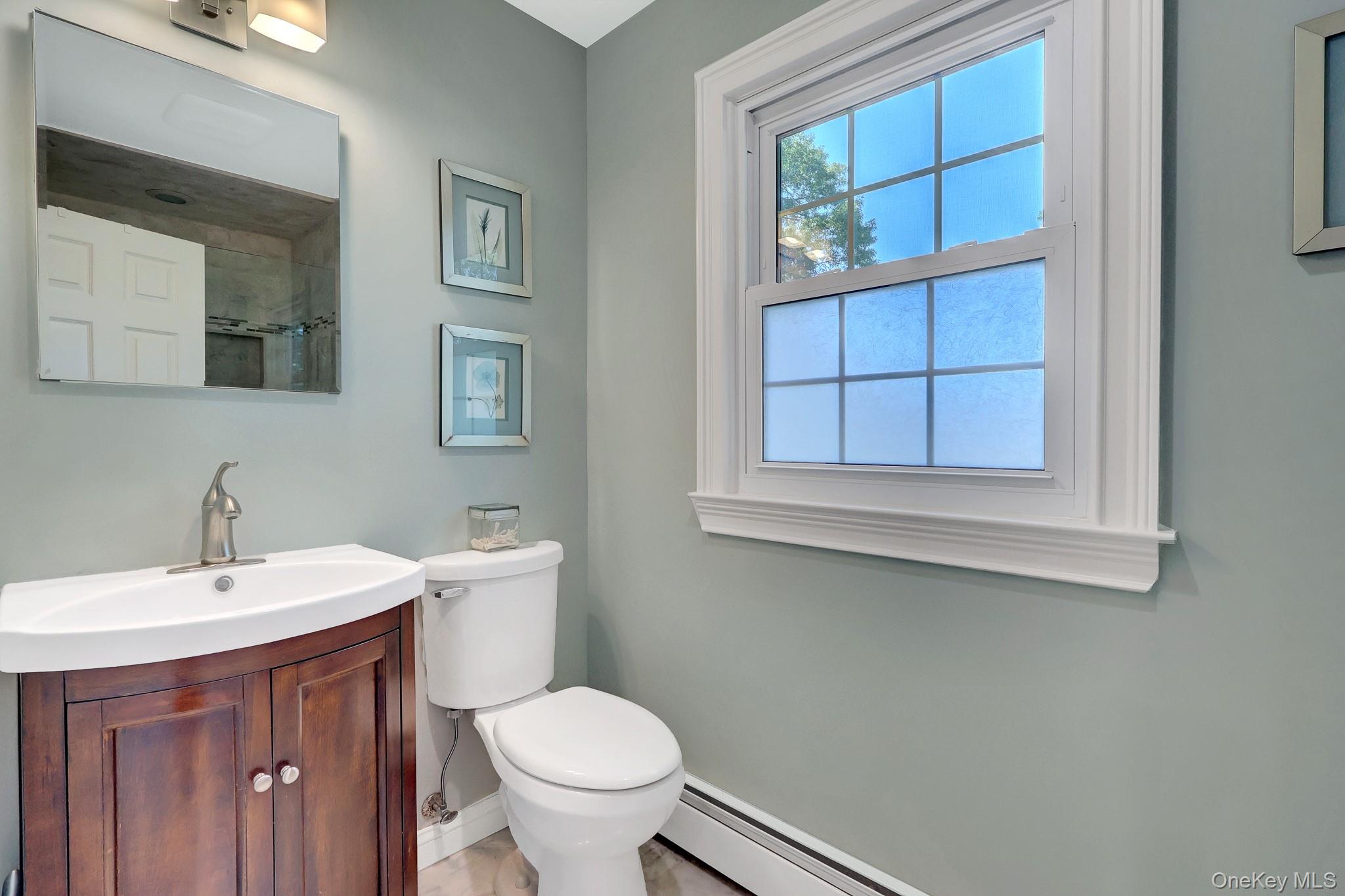 24 Fox Road East Setauket, NY 11733 - Photo 25 of 48 Bathroom featuring a wood-finish vanity with a white basin sink, brushed nickel faucet, and a wall-mounted mirror and radiant heat flooring.