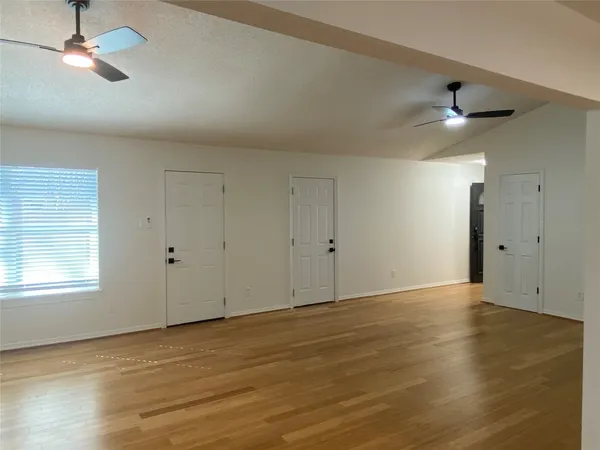 an empty room with wooden floor ceiling fan and windows