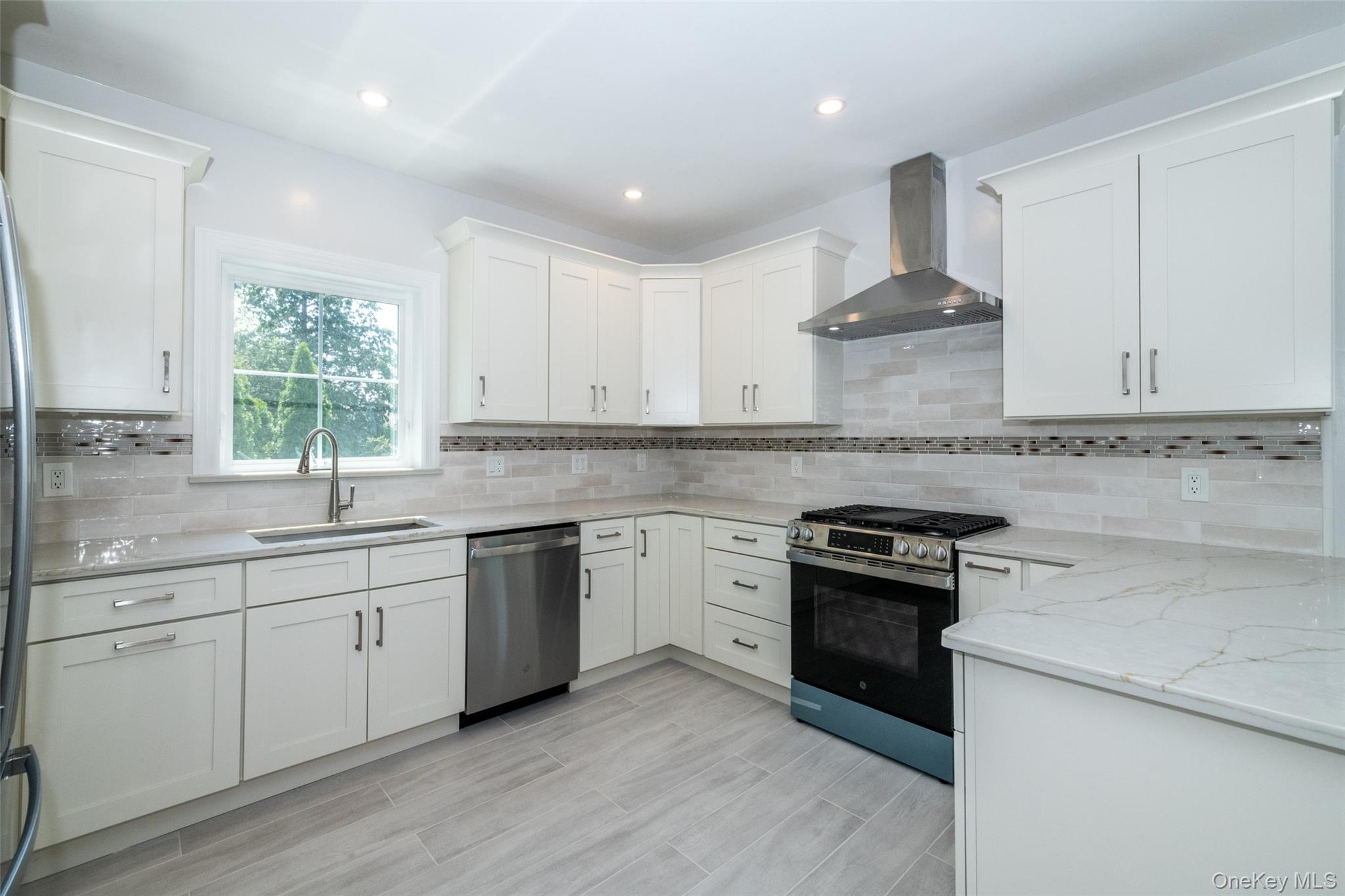 7 Alpha Place, Unit FIRST New Rochelle, NY 10805 - Photo 2 of 25 Kitchen with wall chimney exhaust hood, stainless steel appliances, light stone countertops, white cabinetry, and recessed lighting