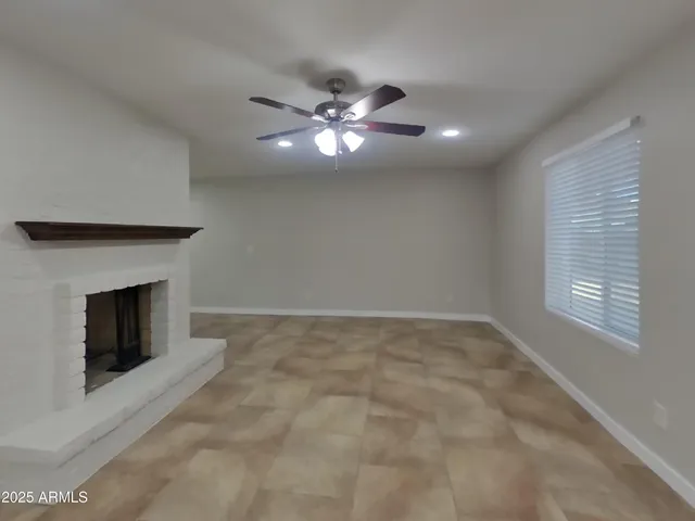 a view of an empty room with chandelier fan and fire place