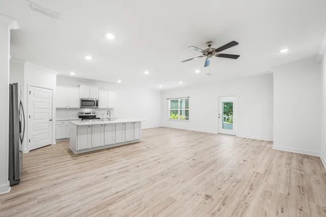 a large kitchen with kitchen island a stove a refrigerator a sink and white cabinets with wooden floor