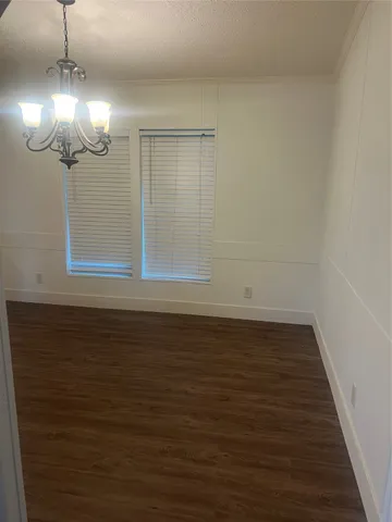 a view of an empty room with wooden floor and a chandelier