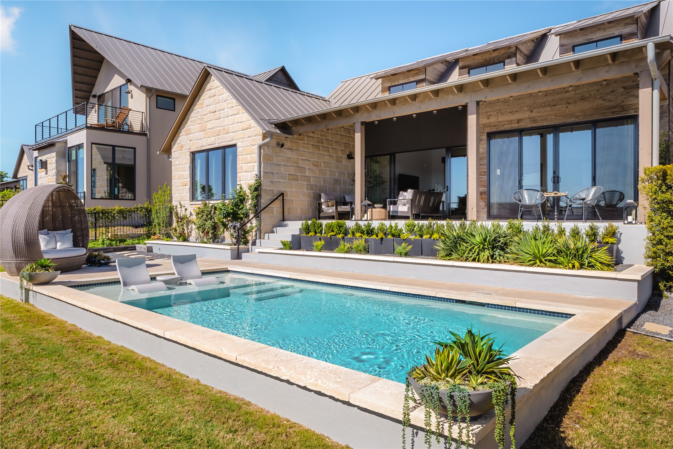 Back of property featuring a patio area, stone siding, a lawn, a balcony, and a standing seam roof