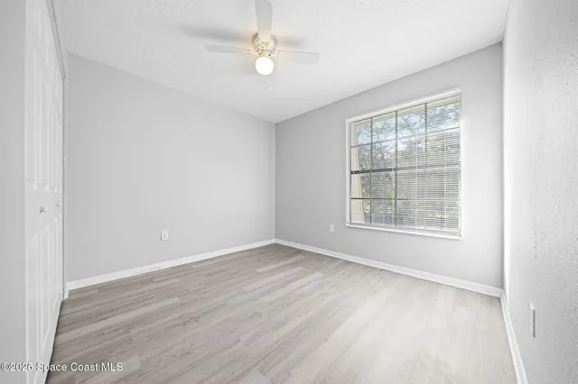 an empty room with wooden floor ceiling fan and windows