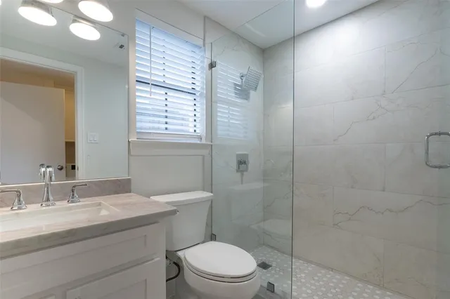 a bathroom with a granite countertop toilet a sink a mirror and shower