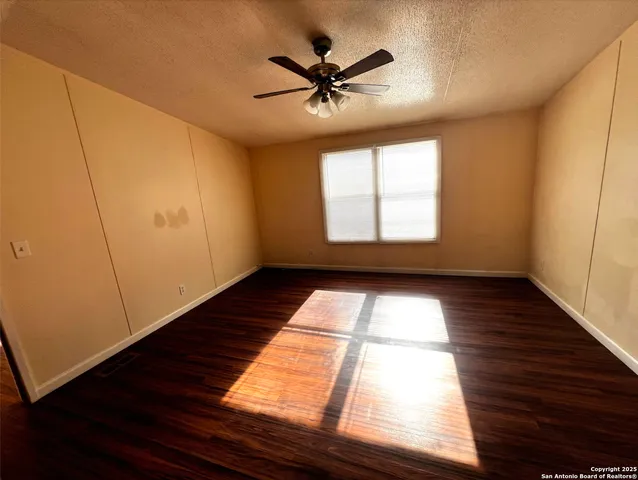 a view of empty room with wooden floor and fan
