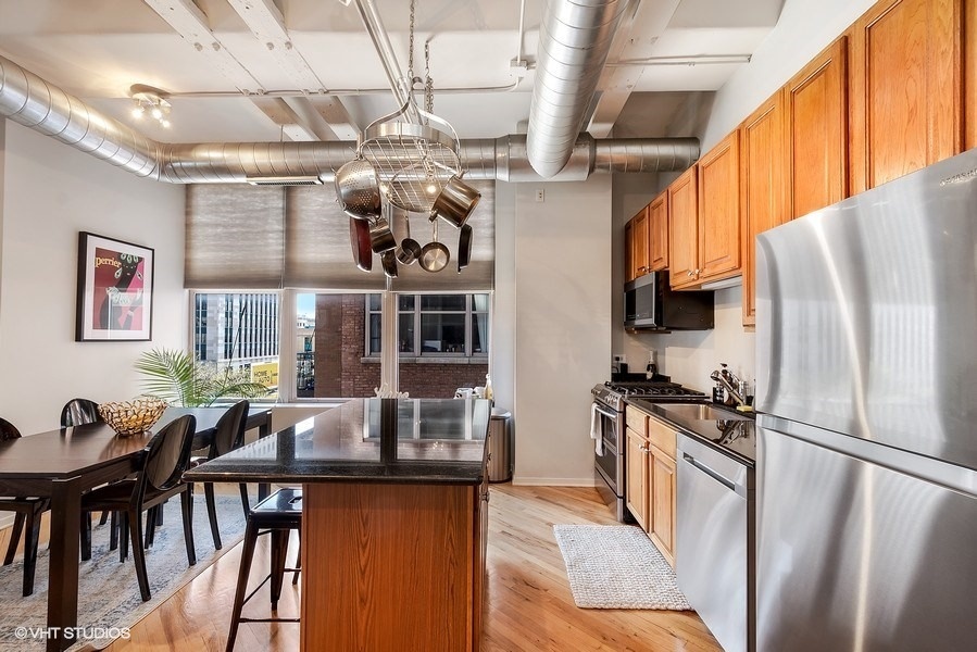 500 South Clinton Street, Unit 404 Chicago, IL 60607 - Photo 16 of 46 a kitchen with stainless steel appliances granite countertop a refrigerator a sink dishwasher a stove and a dining table with wooden floor