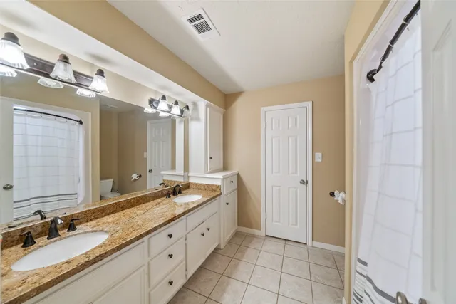 a spacious bathroom with a granite countertop double vanity sink a mirror and a shower