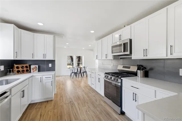 a kitchen with stainless steel appliances granite countertop a stove top oven a sink a refrigerator white cabinets and wooden floor