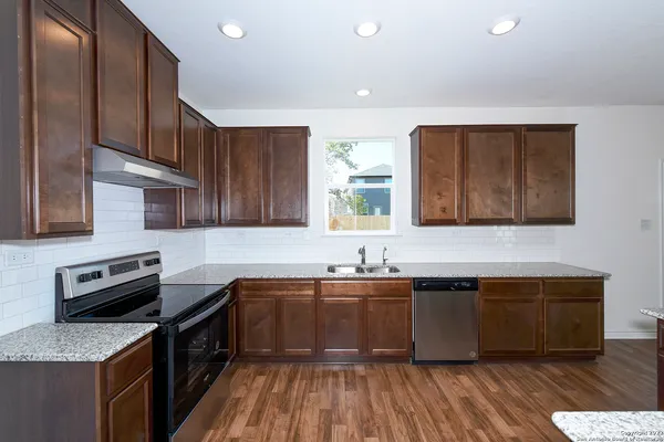 a kitchen with stainless steel appliances granite countertop a sink a stove a refrigerator cabinets and wooden floor