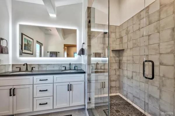 a bathroom with a granite countertop sink two mirror a glass door shower