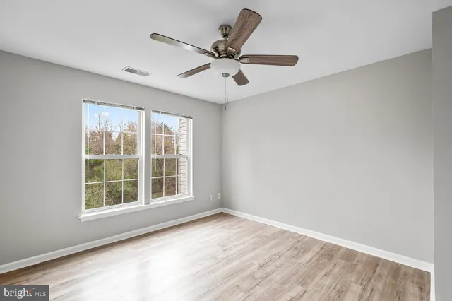 an empty room with wooden floor fan and windows