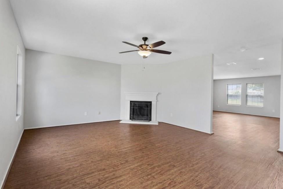 12005 Arbor Lake Road Rhome, TX 76078 - Photo 7 of 22 Unfurnished living room with a glass covered fireplace, a ceiling fan, and wood finished floors