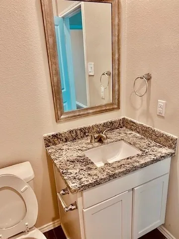 a bathroom with a granite countertop toilet a sink and mirror