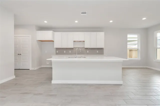 a large white kitchen with a sink dishwasher a stove and white cabinets with wooden floor