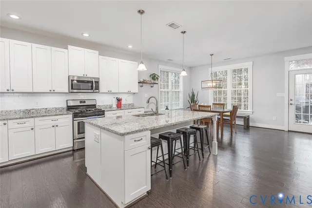 a kitchen with granite countertop stainless steel appliances a stove a sink a dining table and chairs