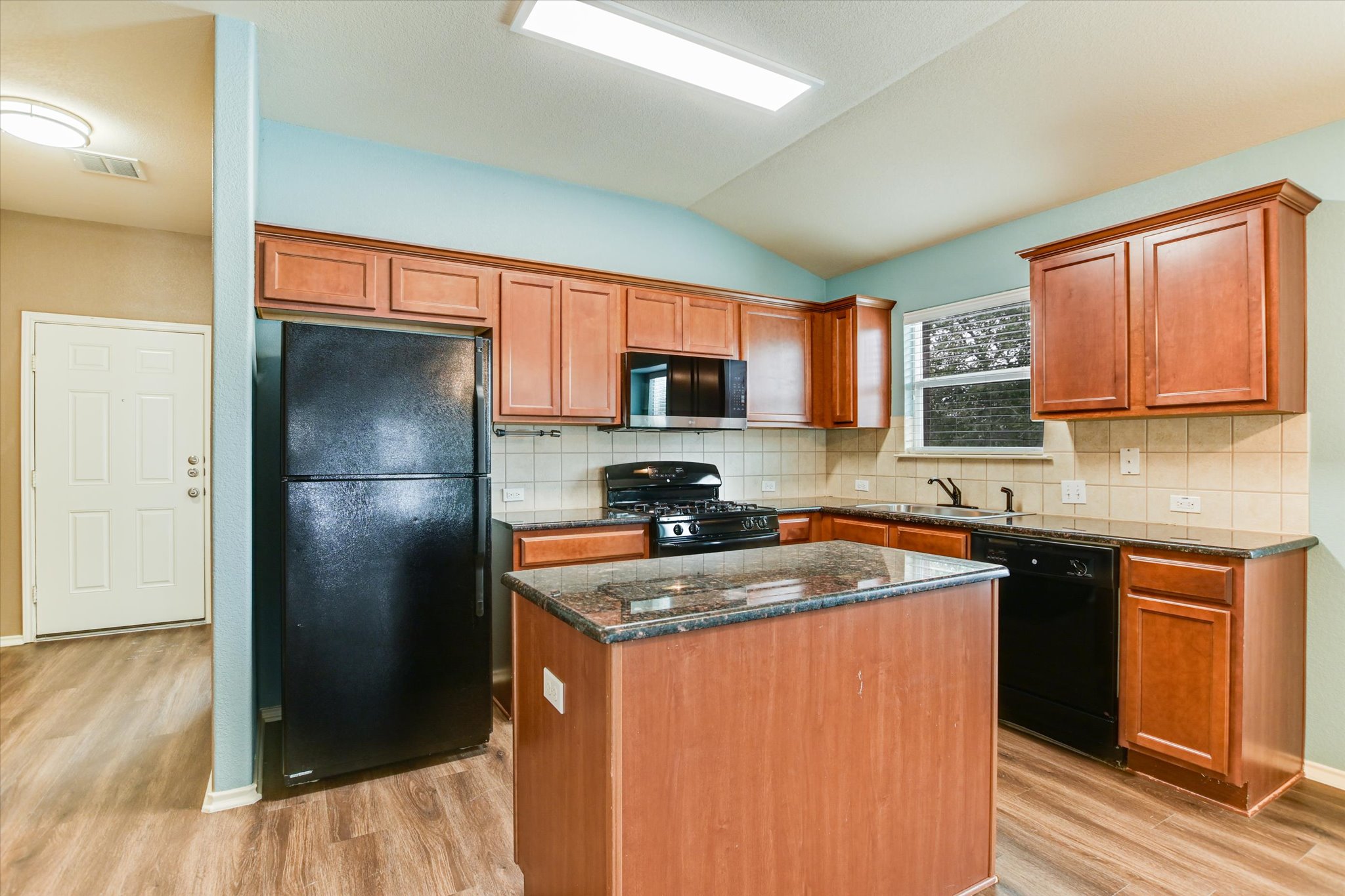 2864 Hearthsong Loop Round Rock, TX 78665 - Photo 5 of 29 Kitchen featuring black appliances, dark stone countertops, a center island, light wood-style floors, and vaulted ceiling