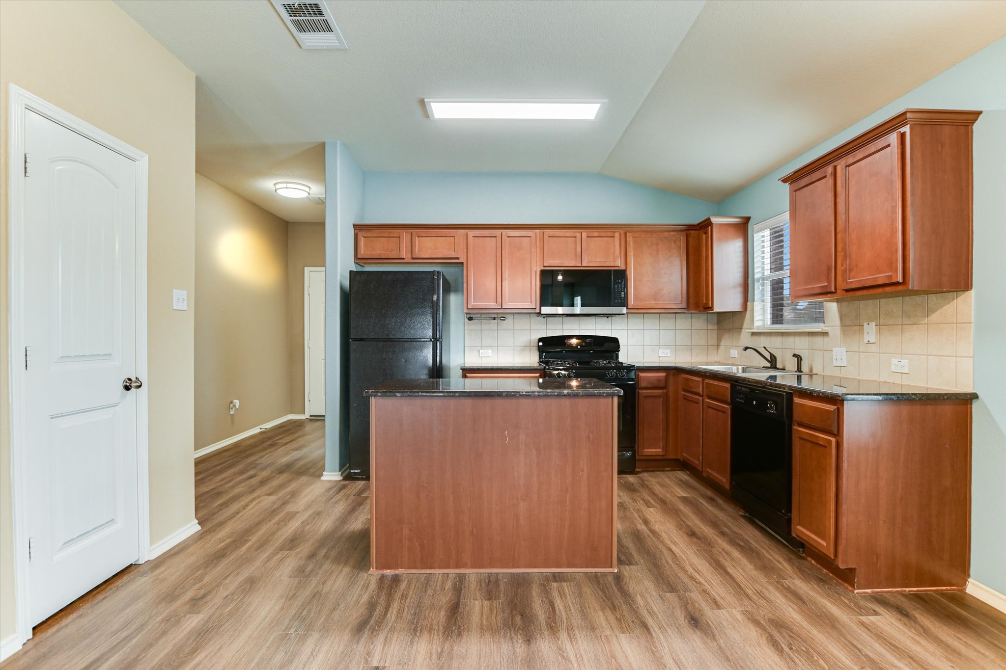 2864 Hearthsong Loop Round Rock, TX 78665 - Photo 7 of 29 Kitchen featuring a kitchen island, black appliances, vaulted ceiling, backsplash, and brown cabinetry