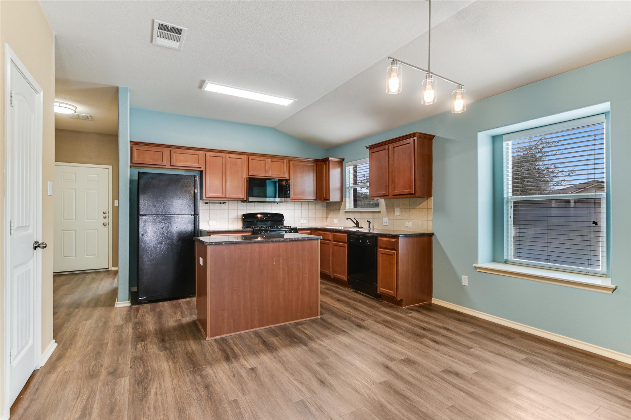 2864 Hearthsong Loop Round Rock, TX 78665 - Photo 8 of 29 Kitchen featuring a kitchen island, black appliances, brown cabinetry, pendant lighting, and vaulted ceiling