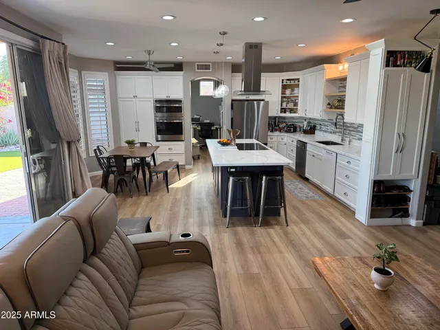 a living room with stainless steel appliances furniture wooden floor and a kitchen view