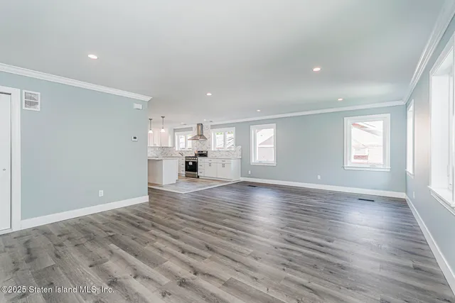 an empty room with wooden floor kitchen view and windows
