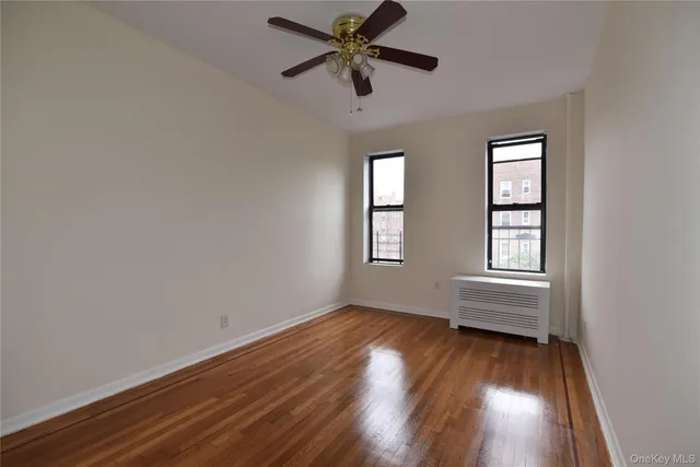 a view of an empty room with wooden floor and a ceiling fan