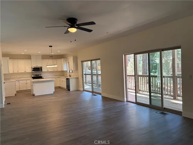 a view of an empty room with wooden floor and a kitchen