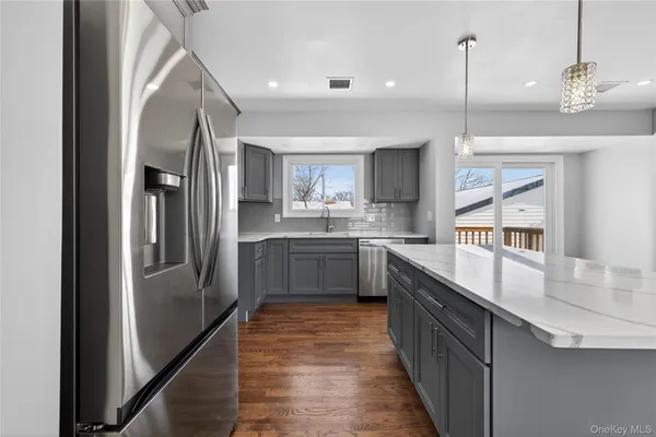 a kitchen with stainless steel appliances granite countertop a refrigerator a sink dishwasher a oven and a dining table with wooden floor
