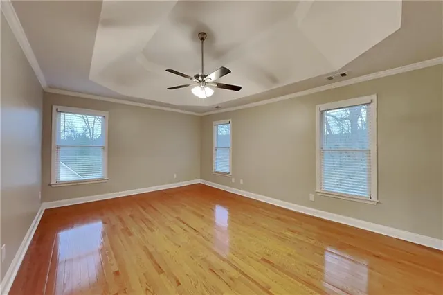 an empty room with wooden floor chandelier fan and windows