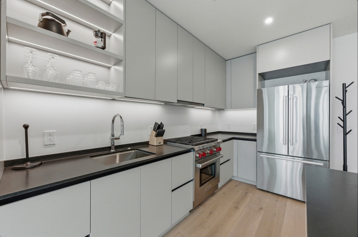 610 Davis Street, Unit 3104 Austin, TX 78701 - Photo 5 of 40 Kitchen featuring open shelves, stainless steel appliances, dark countertops, modern cabinets, and light wood-type flooring