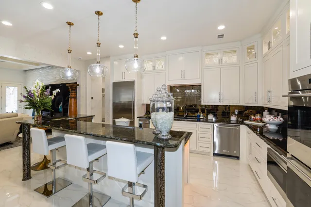 a kitchen with stainless steel appliances kitchen island granite countertop a stove a sink a oven a dining table with chairs and white cabinets