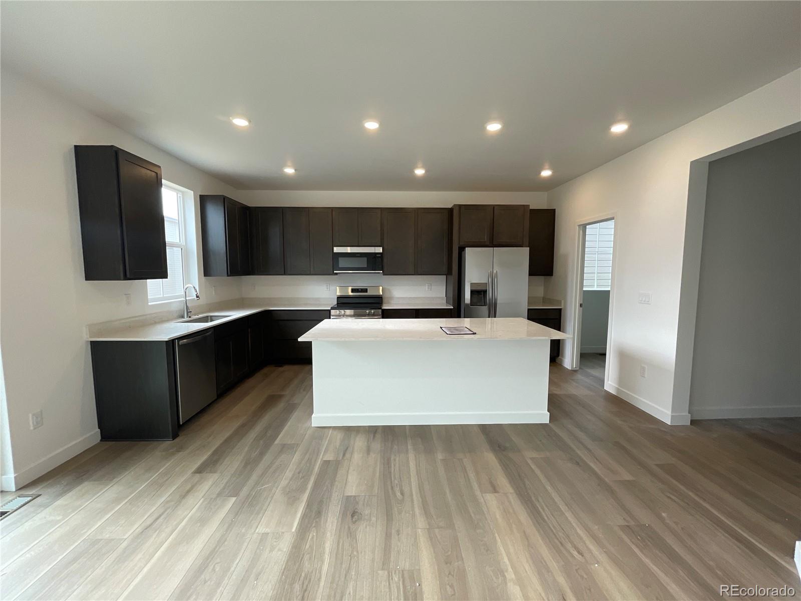 12880 Range Street Firestone, CO 80504 - Photo 2 of 21 a large kitchen with kitchen island a sink dishwasher a refrigerator and a stove with wooden floor