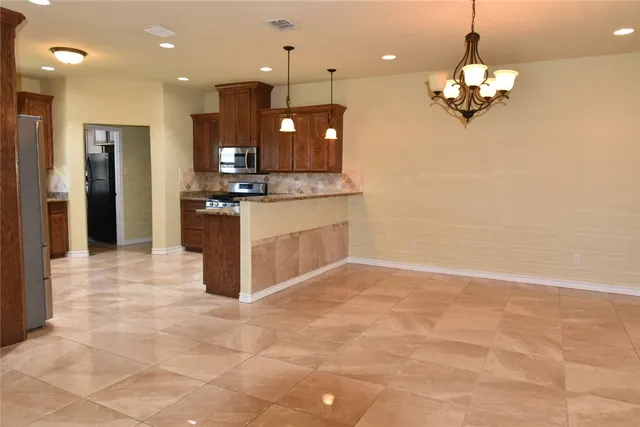 a large kitchen with granite countertop a large kitchen island a sink a refrigerator and a chandelier