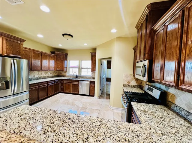 a large kitchen with stainless steel appliances kitchen island granite countertop a refrigerator and a sink