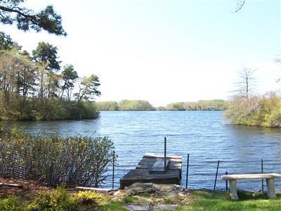 Undisclosed Address Centerville, MA 02632 - Photo 19 of 21 a view of a lake with lawn chairs and a large tree