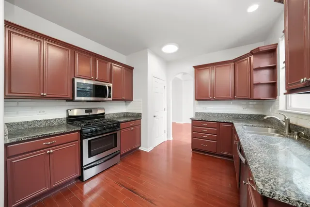 a kitchen with stainless steel appliances granite countertop wooden cabinets a stove a sink and dishwasher with wooden floor