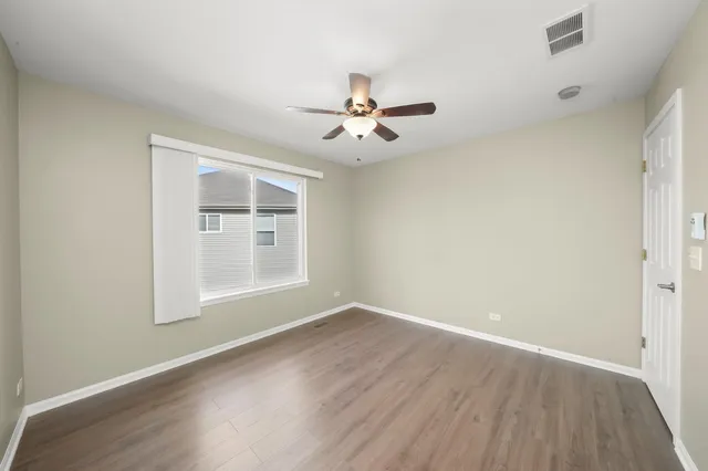 an empty room with wooden floor ceiling fan and windows