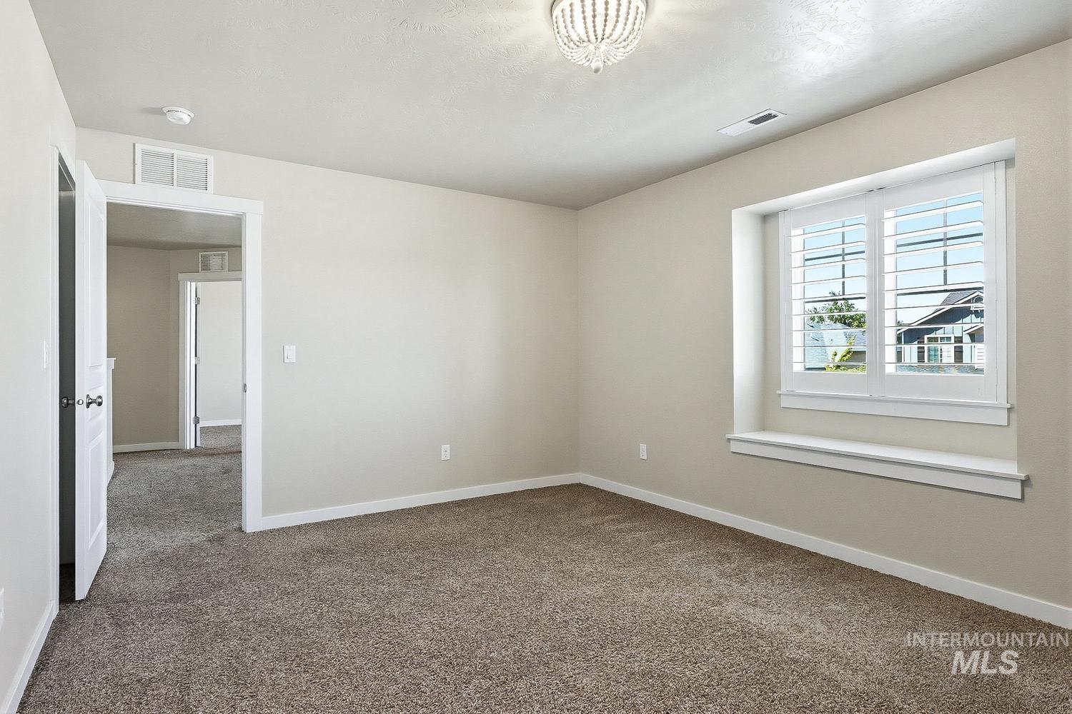846 North Hidden View Way Star, ID 83669 - Photo 38 of 49 Neutral-toned room featuring a large window with white plantation shutters, a decorative chandelier, and textured carpet flooring